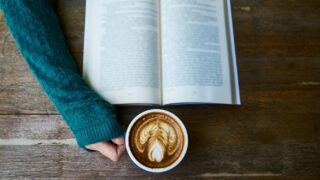 person having cup of latte while reading book