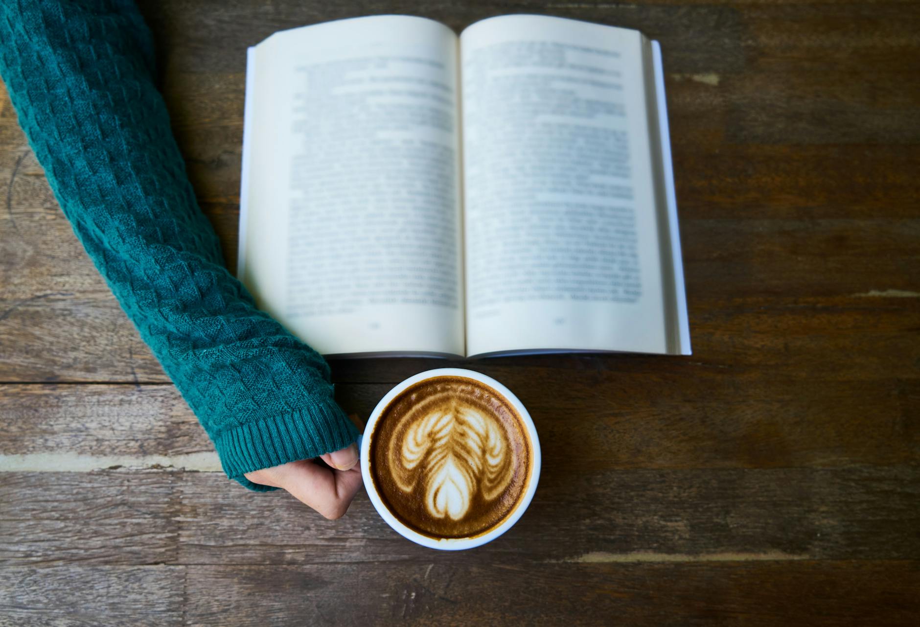 person having cup of latte while reading book